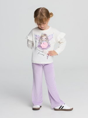 Camicia bianca a maniche lunghe con maniche arricciate, con grafica di una fata. Abbinata a pantaloni flare in velluto a coste color lavanda e sneaker bianche con strisce.