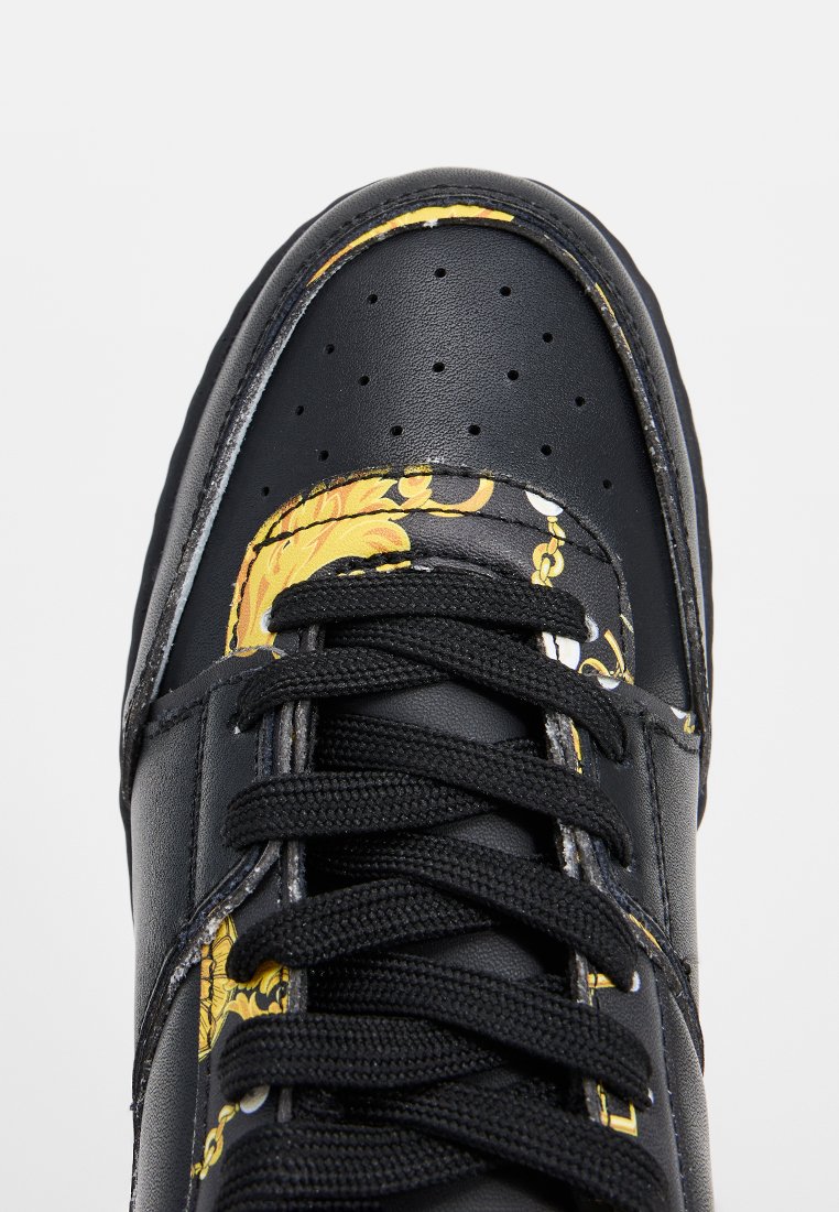 Zapatilla de cuero negro con cordones negros y acentos de patrón floral barroco amarillo en la punta y los lados.