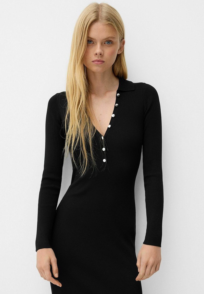 Abito nero a maniche lunghe a coste con scollatura a V e dettagli con bottoni, forma aderente e texture liscia.