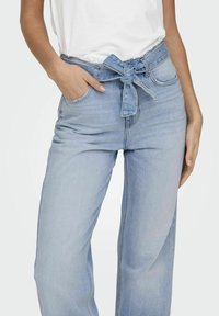 Jasnoniebieskie dżinsy typu wide-leg z wiązanym paskiem w talii, wysoki stan i subtelne przetarcia. Denimski materiał o gładkiej fakturze.