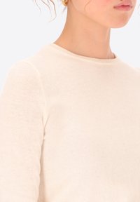  Maglione lavorato a maglia color crema con scollatura rotonda, maniche lunghe e una consistenza morbida. Costine sottili alla scollatura e alle maniche.