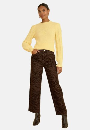Gelber Pullover mit strukturierten Zopfmustern und Herzdetails, kombiniert mit braunen Leoprint-Hosen mit weitem Bein und Absatzstiefeln.