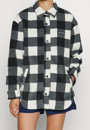 Veste en polaire à carreaux noir et blanc avec boutons-pression, col, poches latérales et logo Columbia sur le côté gauche de la poitrine, portée avec un short bleu marine.