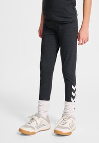 Ciemnoszare legginsy z białym zygzakowatym wzorem po bokach, zestawione z białymi skarpetkami do kostek oraz szarymi trampkami na gumowej podeszwie.