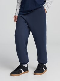 Granatowe spodnie dresowe o luźnym kroju, z elastycznym pasem i bocznymi kieszeniami. Połączone z czarnymi trampkami z białymi paskami.