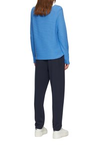 Blauwe geribbelde trui met een ronde zoom, gecombineerd met donkerblauwe broeken en witte platform sneakers, die een relaxte fit laten zien.