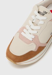 Sneaker met een mix van beige, roze en bruine suède en leer, met witte veters en branding aan de zijkant.