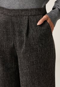 Grau strukturierte Hose mit gefaltetem Vorderteil, seitlichen Taschen und einem glatten Bund. Der Stoff weist ein dezentes punktiertes Muster auf.