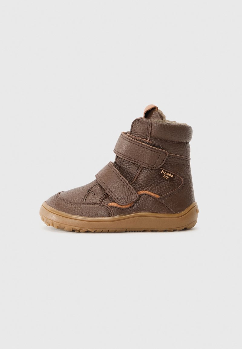 Botte enfant en cuir marron avec deux bandes velcro et une semelle en caoutchouc beige, vue de profil sur un fond clair uni.