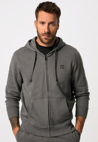 Sudadera gris con cremallera hecha de una tela suave. Cuenta con un bolsillo delantero, capucha ajustable con cordón y un pequeño logo en el pecho.