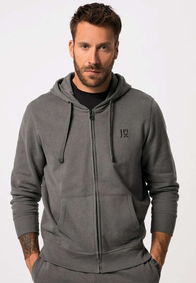Felpa grigia con zip realizzata in tessuto morbido. Presenta una tasca frontale, un cappuccio regolabile con cordino e un piccolo logo sul petto.