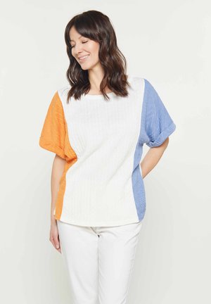 Kleur geblokte gebreide top met oranje, witte en blauwe secties. Korte mouwen, relaxte pasvorm en textuurstof. Gecombineerd met witte broeken.