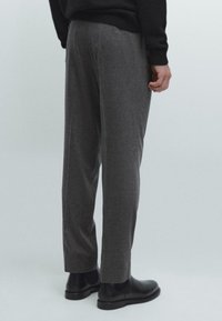 Pantaloni grigi con una texture, dal taglio rilassato, con gamba dritta e vita. Abbinati a stivali neri alla caviglia.