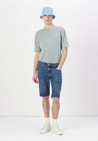 Svijetlosivi pamučni majica, plavi bucket šešir, plave traperice, bijele tenisice. Ležeran outfit s jednostavnim dizajnom i opuštenim krojem.
