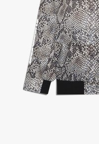 Snakeskin-patterned bomber jacket with a black ribbed hem, featuring a smooth texture and white accents on the sleeves.