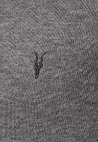 Grauer Strickpullover mit einem dezenten schwarzen gestickten Ziegenlogo auf der linken Seite. Die Textur ist glatt mit einer weichen Oberfläche.