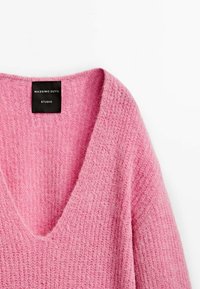 Różowy sweter z dekoltem w serek, wykonany z włóczki o miękkiej, puszystej teksturze, z metką "MASSIMO DUTTI STUDIO". Krawędzie są prążkowane dla dodania szczegółów.