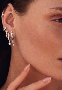 Orecchini esposti in vari design, caratterizzati da metallo argentato, perle e gemme scintillanti. Le forme includono cerchi e elementi pendenti.