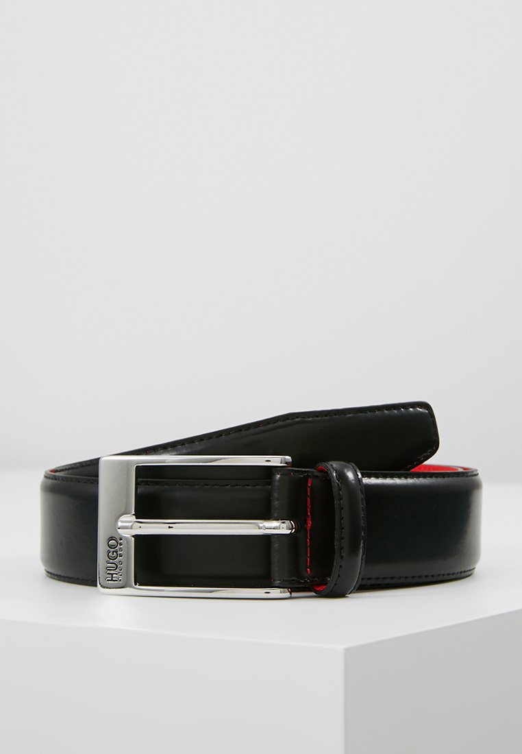 Cinturón de cuero negro con un acabado brillante, hebilla de metal plateado, detalles de costura roja y un diseño de hebilla rectangular.