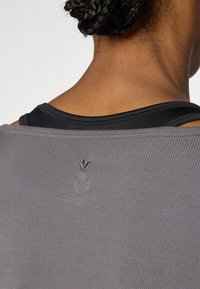 Grå ribbestrikket overdel med et svart innerlag, med en liten logo sydd nær nakken bak.