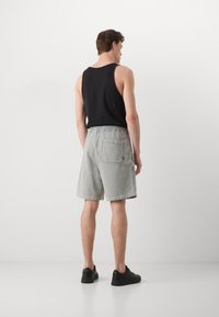 Top negro sin mangas combinado con pantalones cortos gris claro que cuentan con una cintura elástica y un bolsillo trasero. Usado con zapatillas negras. Look simple y casual.