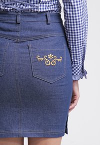 Gonna in denim di colore blu scuro con taglio aderente, caratterizzata da un design ricamato in oro sulla tasca posteriore. Include due tasche posteriori e spacchi laterali.