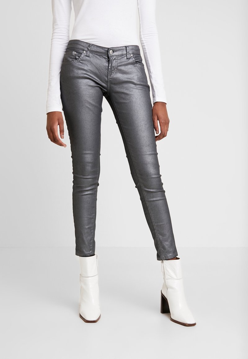 Jean skinny gris métallique à texture lisse, avec poches avant et fermeture éclair à glissière, associé à des bottines blanches à la cheville.