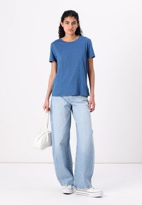 Blå t-skjorte med korte ermer laget av lett stoff, kombinert med lyseblå vide jeans og en hvit håndveske. Minimalistisk design, uformell passform.