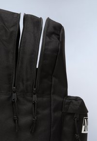 Zaino in tessuto nero caratterizzato da numerised zippers, materiale testurizzato, corde regolabili e una tasca laterale con dettagli del logo.