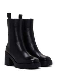 Botas negras hasta el tobillo hechas de cuero suave, con tacón de bloque y suela gruesa. Cuenta con tiradores para facilitar su uso.