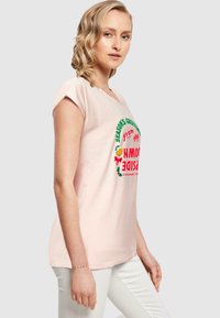 Ljusrosa bomullströja med korta ärmar. Har färgglad text som säger "Säsongens hälsningar från Upside Down" och festliga detaljer.