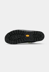 Sola de Vibram com cravos profundos e multidirectionais; borracha preta com detalhes amarelos; projetada para tração e durabilidade em vários tipos de terrenos.