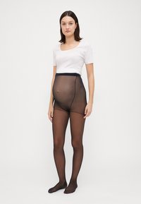 Svart graviditetstights med et semi-transparent design, h�øy midje og glatt tekstur, kombinert med en tettsittende hvit T-skjorte med korte ermer.