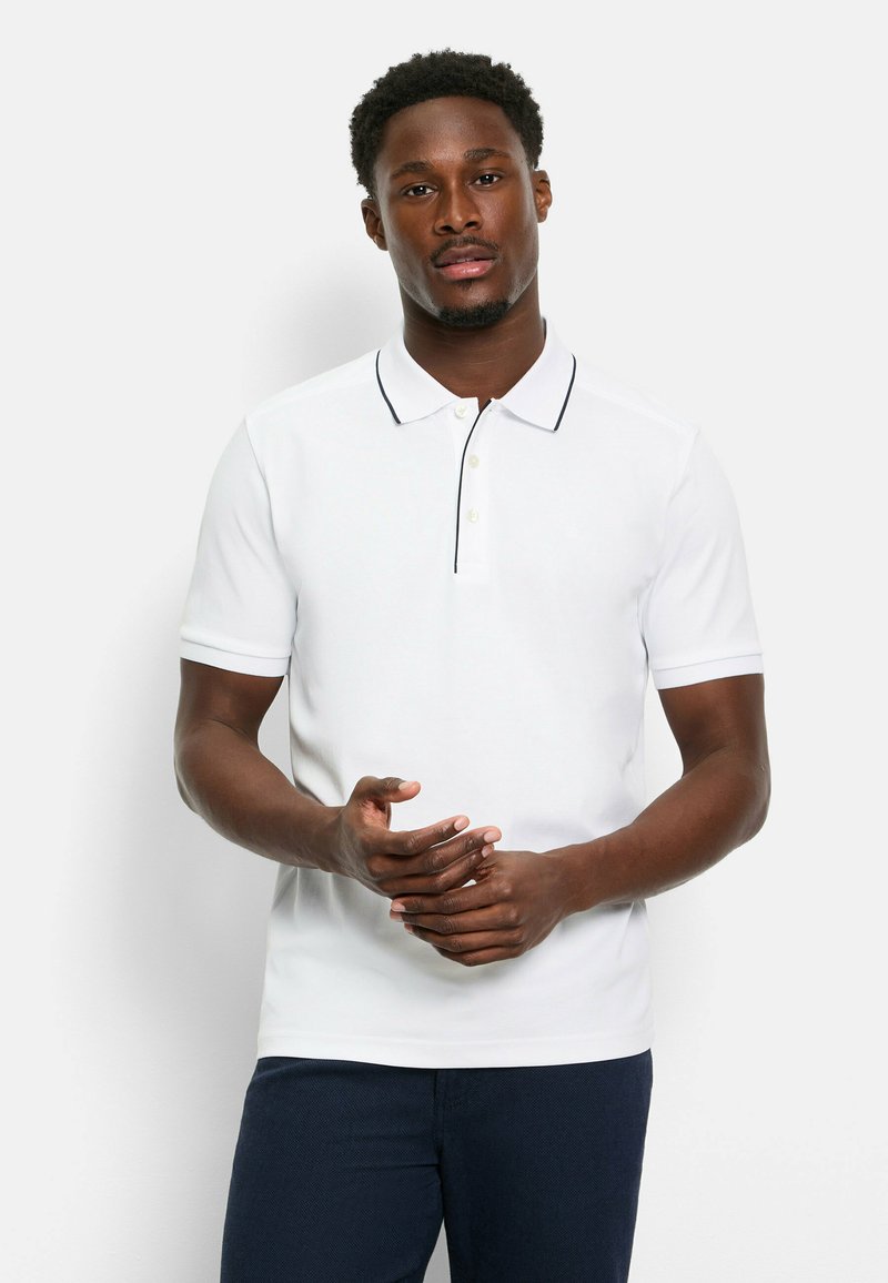 Weißes Poloshirt mit einer Knopfleiste mit zwei Knöpfen, schwarzer Paspelierung entlang des Kragens, kurzen Ärmeln und glatter Textur. Getragen mit dunkelblauen Hosen.