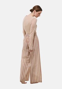 Haut beige à manches longues associé à un pantalon à larges jambes rayé rose et beige. Le pantalon présente une taille froncée et un tissu doux.
