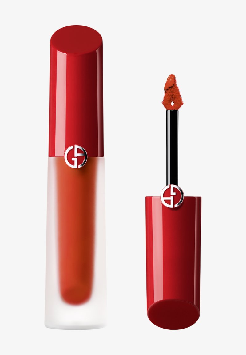 Czerwona pomadka w płynie w przezroczystym szklanym pojemniku, z błyszczącą czerwoną zakrętką z metalowym logo, obok aplikatora z puszystym końcem.