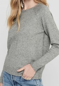 Maglione grigio lavorato a maglia con scollatura a girocollo, maniche raglan e orlo a coste. Morbida texture, silhouette aderente e dettagli di design minimali.