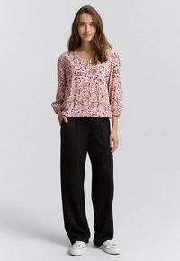 Šviesiai rožinė, tekstūruota palaidinė laisvo silueto su V formos iškirpte. Derinama su juodomis, plačiomis kelnėmis ir baltais sportbačiais.