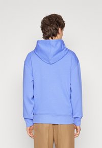 Ljusblå hoodie med en känguruficka, långa ärmar, framsömnadsdetaljer och en huva med dragsko, parat med bruna byxor.