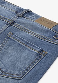 Jeans in denim blu con una finitura sbiadita, caratterizzati da cuciture gialle a contrasto, una piccola tasca posteriore e un'etichetta in pelle marrone sulla vita.
