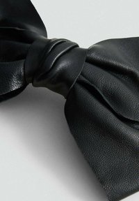 Fiocco in pelle nera con trama dettagliata legato al centro su uno sfondo grigio chiaro uniforme.