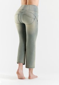 Jeans capri verde sbiaditi con una silhouette aderente, dotati di tasche posteriori curve e dettagli in hardware argentato. Tessuto morbido e strutturato.