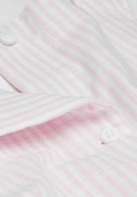 Weißer Stoff mit rosa Streifen, ausgestattet mit zwei weißen Knöpfen. Die Textur wirkt leicht und leicht durchsichtig.