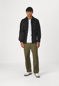 Camisa negra de botones, camiseta blanca, pantalones verde oliva y zapatillas claras con detalles en negro. Bolsa cruzada negra con cremallera.