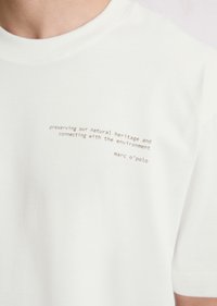 White cotton t-shirt featuring a crew neckline and printed text in brown. Text reads about natural heritage and the brand name, marc o’polo.