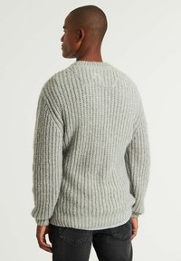 Hellegrauer Strickpullover mit gerippter Textur, langen Ärmeln, Rundhalsausschnitt und kontrastierenden Nähdetails am Rücken.