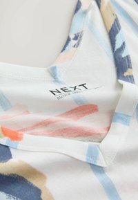 Close-up af en flerfarvet slouch-kjoles udskæring med NEXT-mærket og blødt pastel abstrakt mønster.