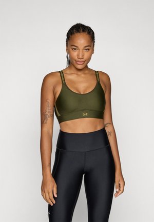 Olivengrønn sports-bh med rund halslinning og justerbare stropper med svart merkevare. Kombinert med høyt liv sorte leggings.