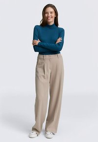 Maglia a collo alto turchese abbinata a pantaloni beige a gamba larga a vita alta e sneakers bianche. Tessuto liscio e design semplice.