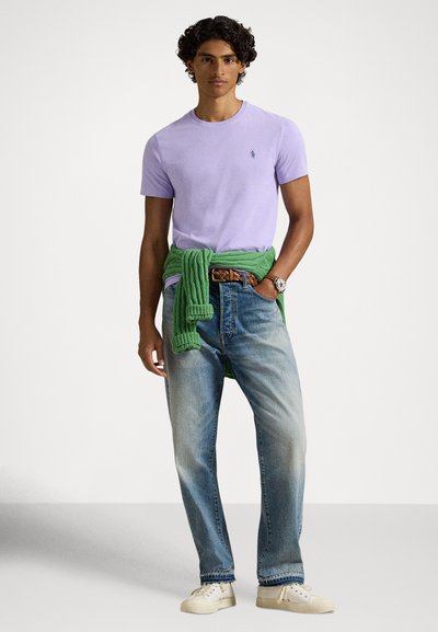 Fialové tričko stredného strihu, kombinované so svetlomodrými džínsami. Zelený sveter zviazaný v páse, béžové topánky, strieborné hodinky na zápästí.